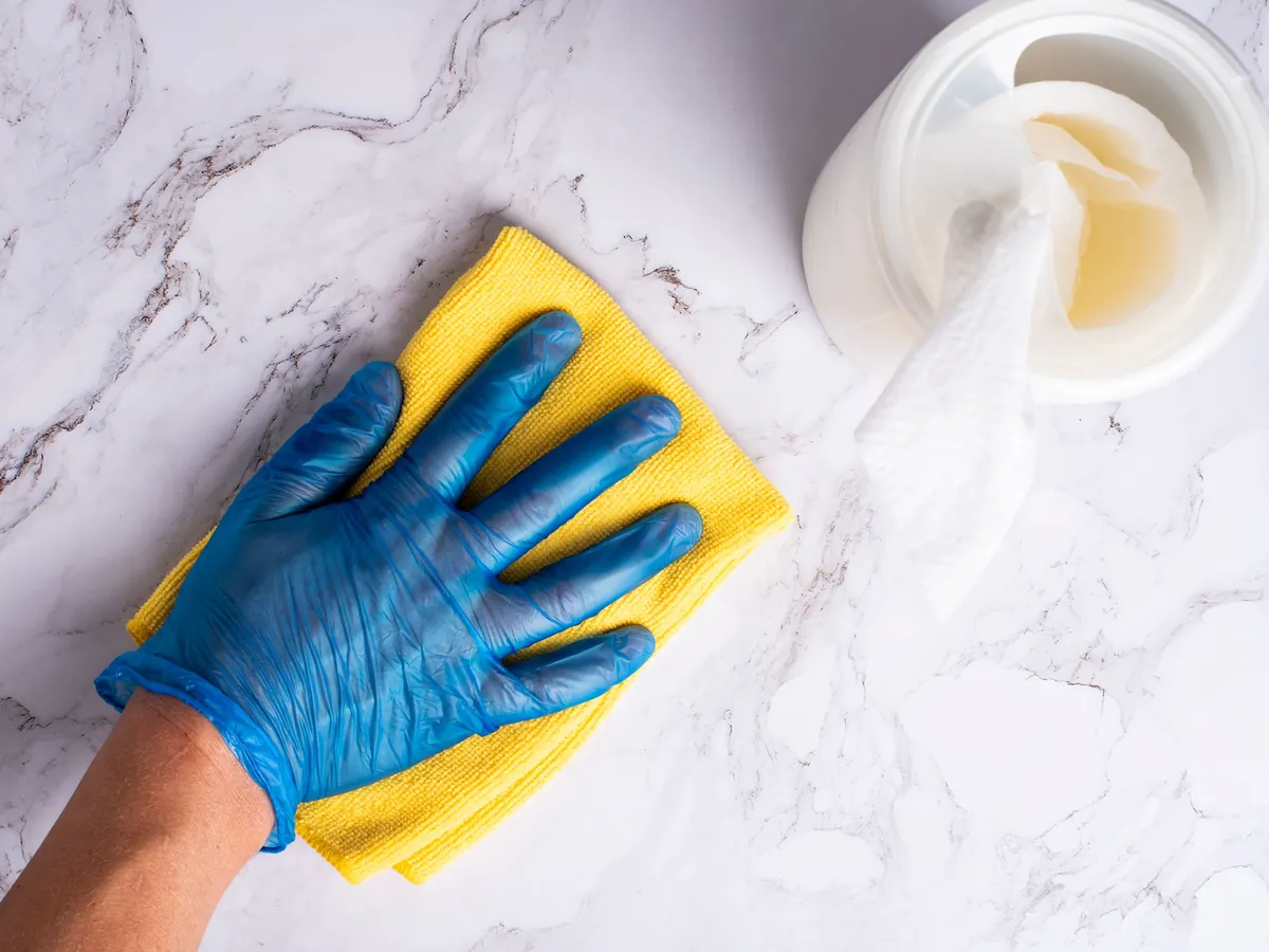 A gloved hand wiping a marble countertop with a yellow cloth