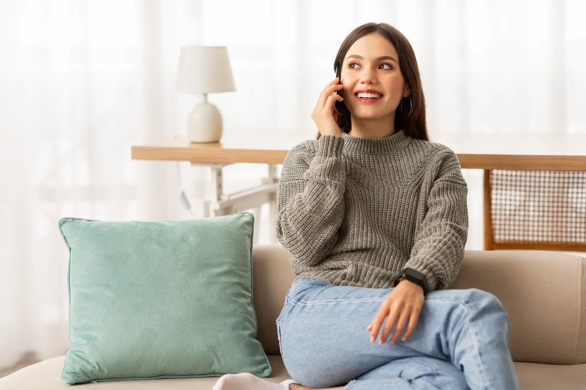 A smiling woman talking on the phone on a sofa at home