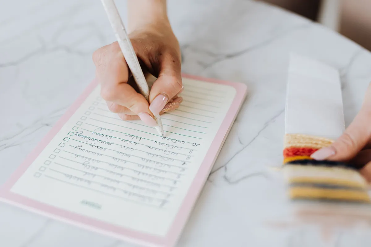 A hand filling in a cleaning checklist next to cleaning sponges
